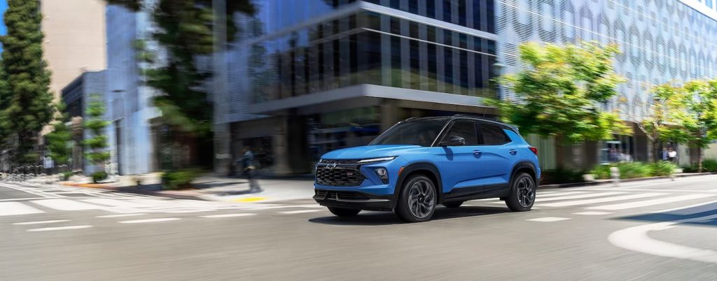 A blue 2024 Chevy Trailblazer RS is shown driving through a city after viewing Chevy SUVs for sale.