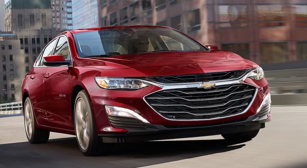 A red 2025 Chevy Malibu 2LT is driving through a city to a Chevy dealer near Natchitoches.