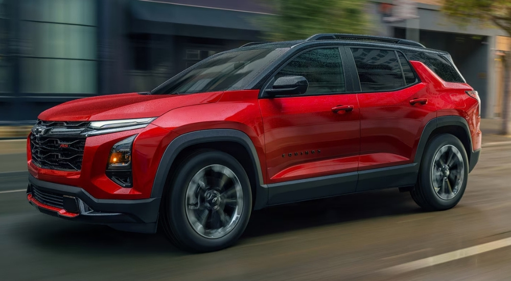 A red 2025 Chevy Equinox for sale in Alexandria is driving past shops.