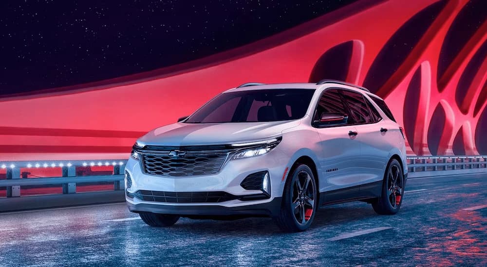 A red 2024 Chevy Equinox Premier Redline for sale is shown driving on a bridge illuminated with red lights.