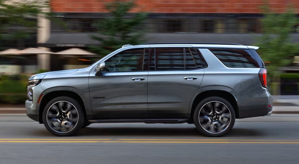 A grey 2025 Chevy Tahoe for sale is driving on a city street.