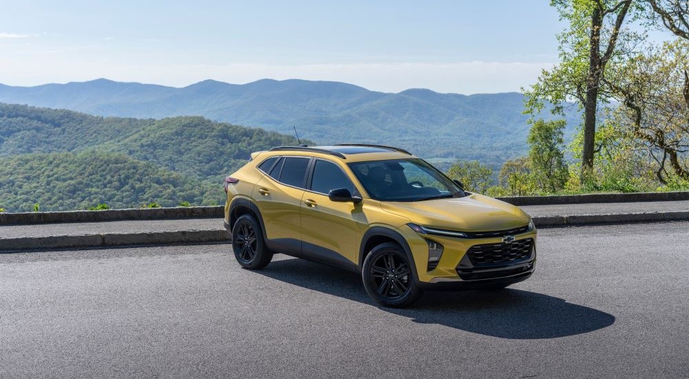 A popular Chevy Trax for sale, a yellow 2024 Chevy Trax Activ, is shown overlooking mountains.