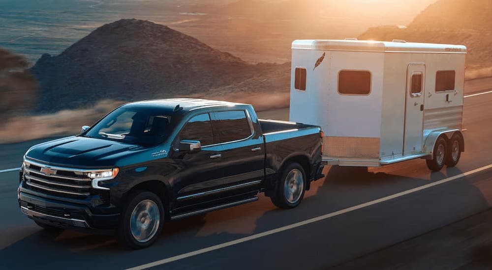 A black 2022 Chevy Silverado 1500 High Country is towing a white enclosed trailer.