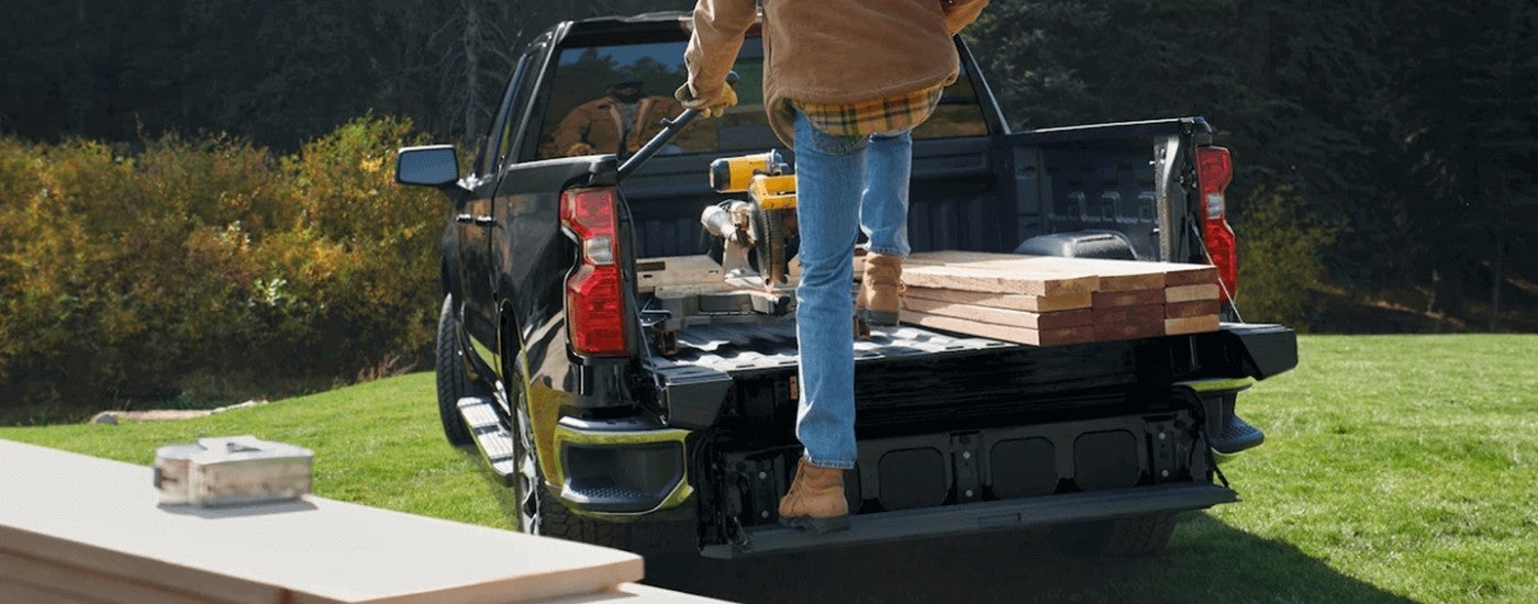 A man stepping on the liftgate of a black 2022 Chevy Silverado 1500.