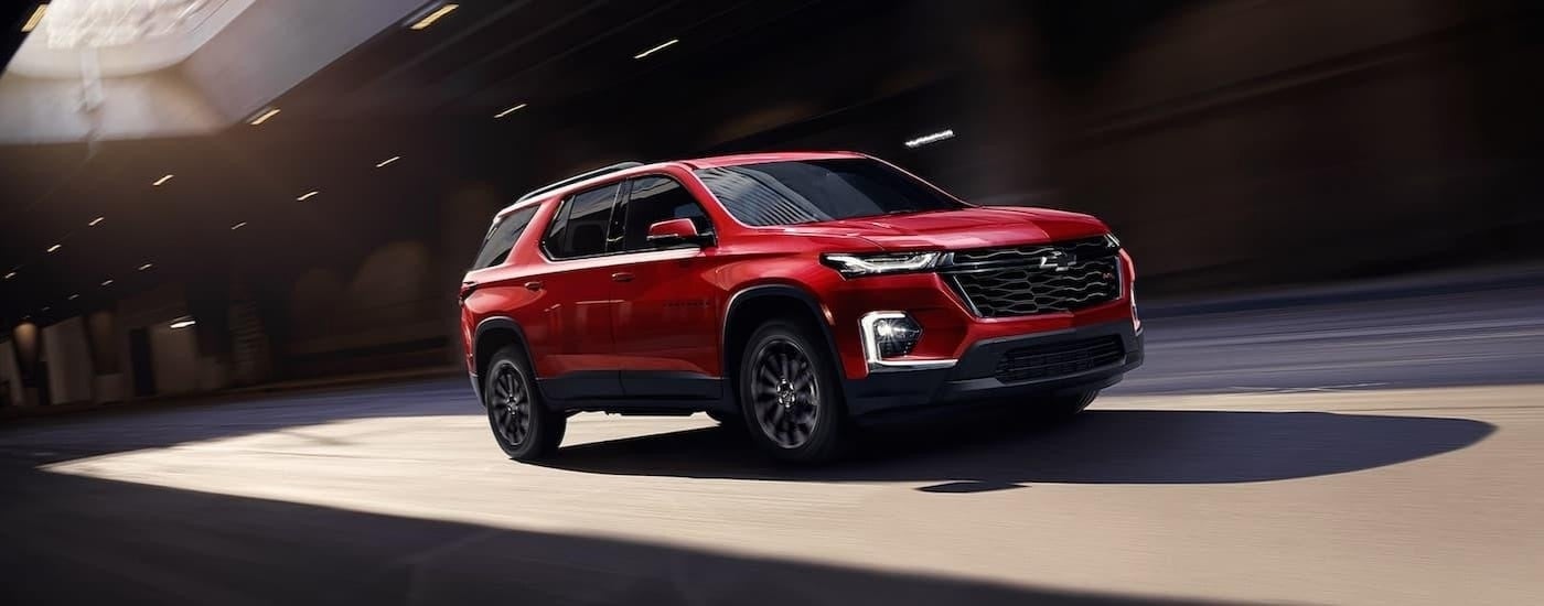 A red 2023 Chevy Traverse RS driving to a Chevy dealer.