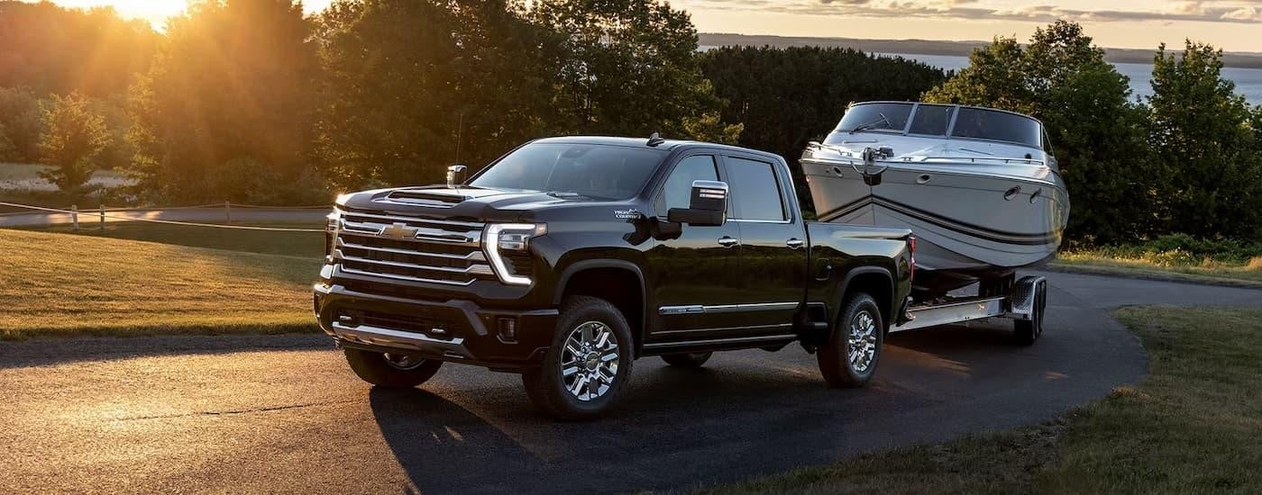 A black 2024 Chevy Silverado 2500HD High Country is towing a boat on a winding road.