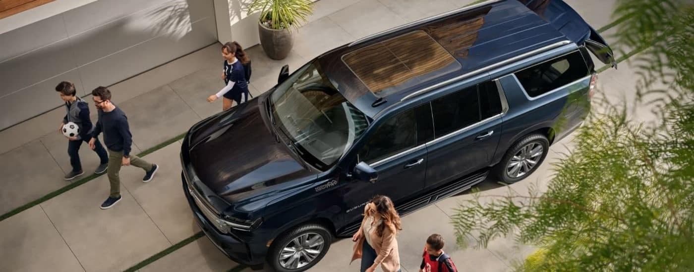 A blue 2023 Chevy Suburban parked near a family.