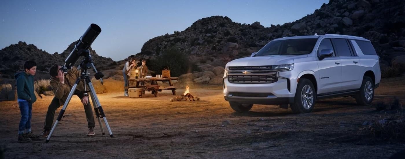 People are shown using a telescope near a white 2023 Chevy Suburban.