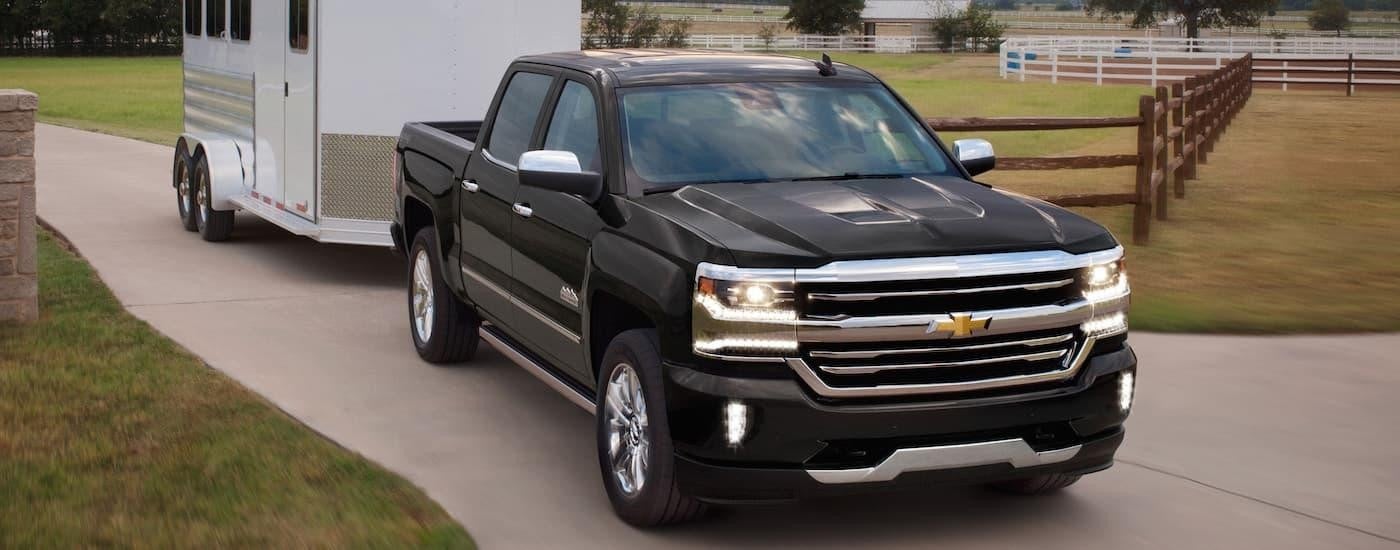 A black 2018 Chevy Silverado 1500 is shown towing a white enclosed trailer past fences.