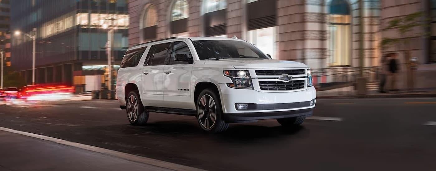 A white 2020 Chevy Suburban is shown driving on a city street after leaving a used Chevy dealership.